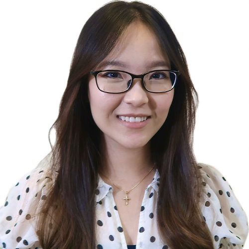 Portrait of a smiling woman with long dark hair and black glasses, wearing a white polka-dot blouse.